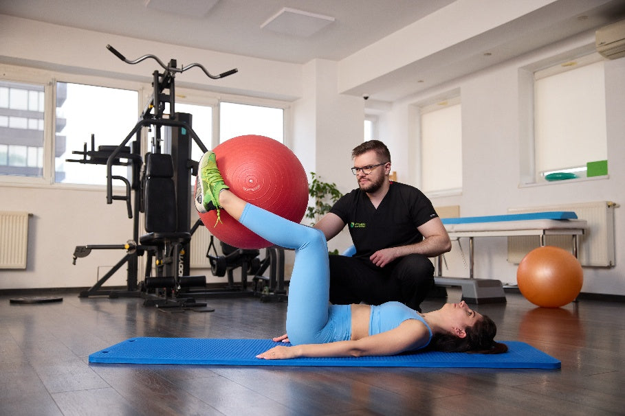 Physiotherapist assisting a patient with a large exercise ball in a clinic setting.